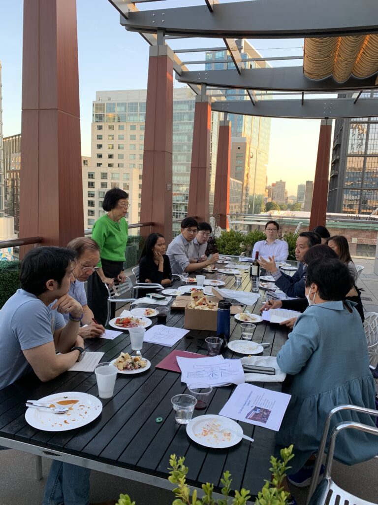 Foundation members seated around a long table at an outdoor rooftop meeting, with the city skyline behind them