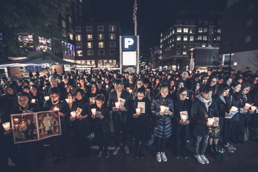 A large crowd fills a city square at night, each person holding a lit candle; several hold framed portraits